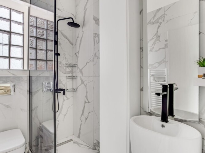 Halu! Elegant modern bathroom featuring marble tiles a sleek black shower fixture and a stylish basin. Bright natural light enhances the clean and minimalist design.