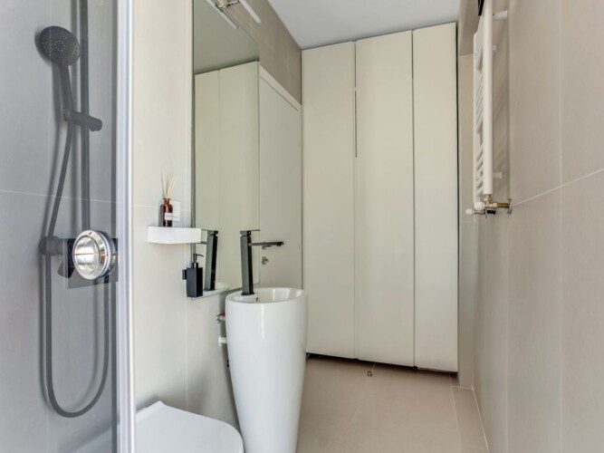 Halu! Modern minimalist bathroom with sleek shower enclosure and contemporary sink. The space features elegant floor-to-ceiling cabinets for efficient storage.