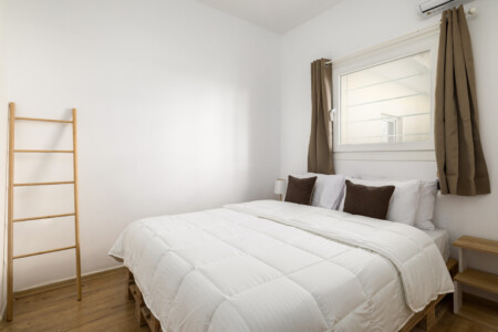 Halu! Cozy bedroom at Ourania Lofts and Suites in Thessaloniki featuring a comfortable double bed with white bedding natural light and modern minimalist decor.