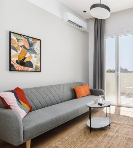 Halu! Modern living room with a gray sofa accented by colorful pillows contemporary artwork on the wall natural light from a large window and a round coffee table