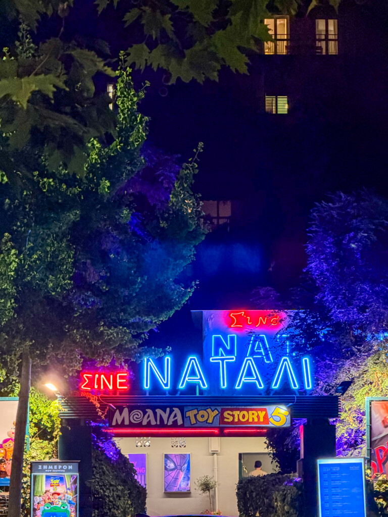 Neon entrance of Natali open air cinema in Thessaloniki, surrounded by trees on a summer night.
