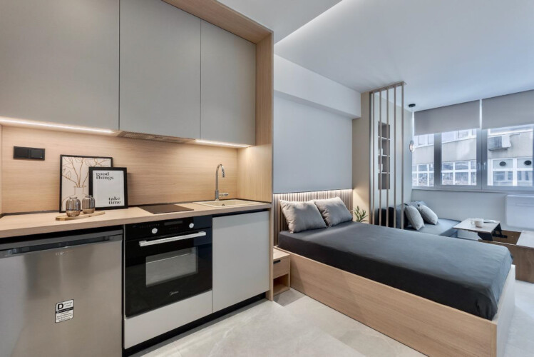 Halu! Explore the modern interior design of Odyssey - Premium SKG Suites in the heart of Ladadika Center featuring a cozy bed and stylish kitchen area.